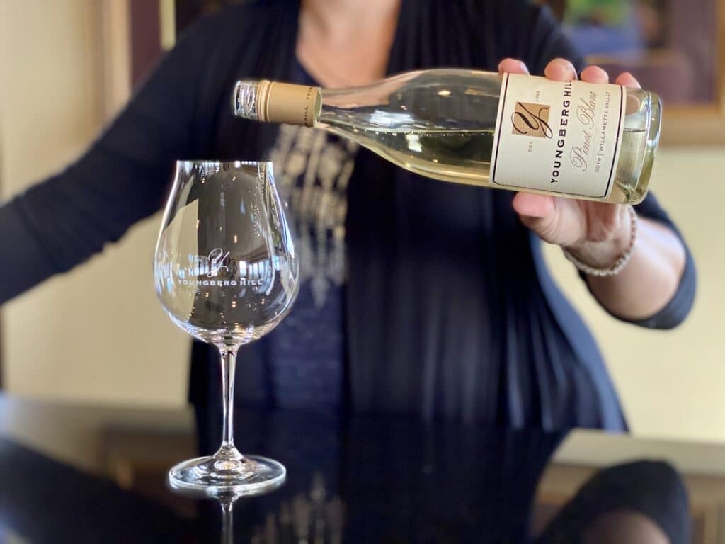 10 Best Wineries in the Willamette Valley to Try in 2023, photo of the Youngberg Hill winery tasting room, a woman pouring a white wine 