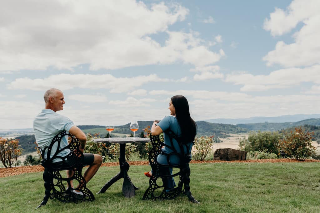 Things to do in McMinnville, photo fo the stunning view at youngberg hill, couple sitting with a glass of wine